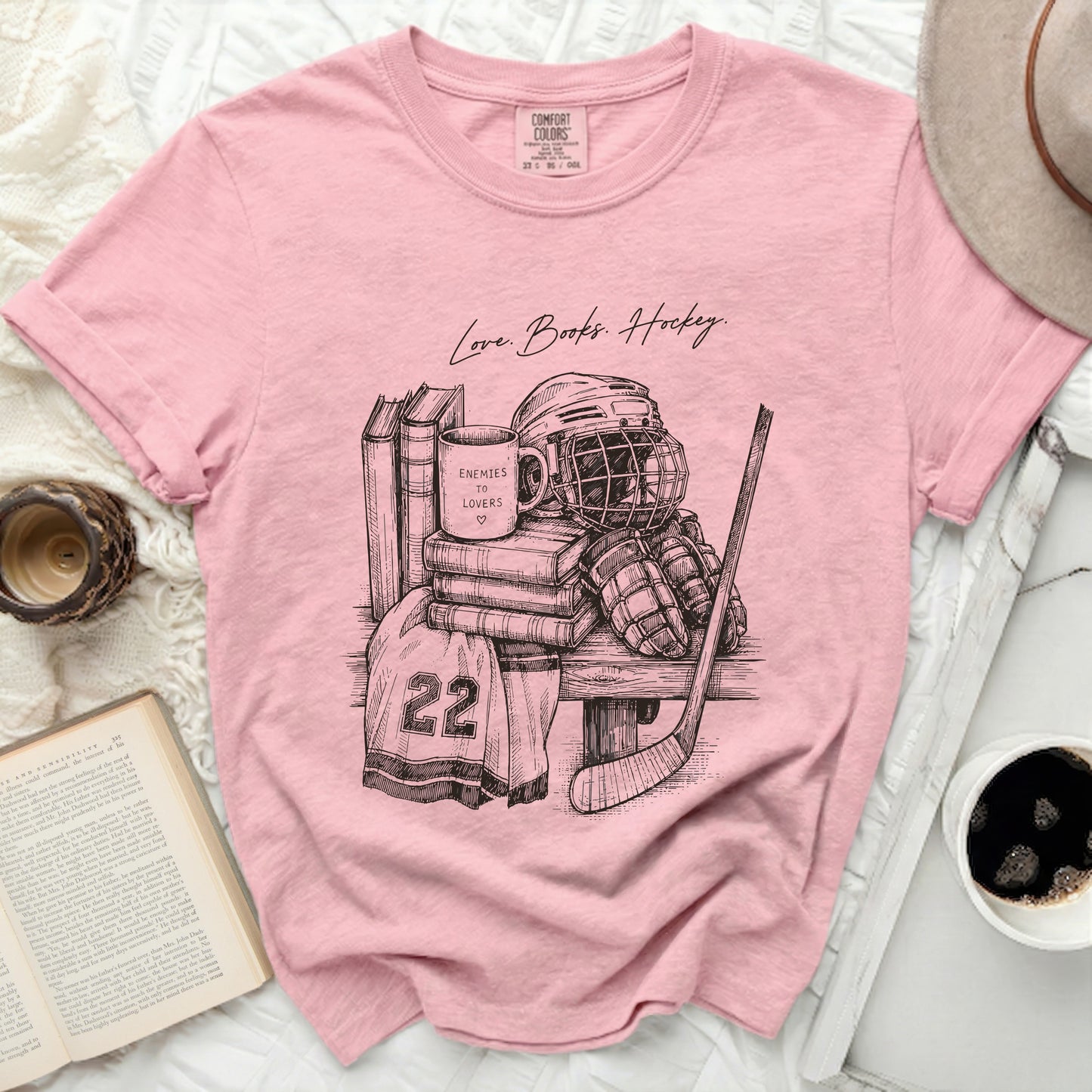 Pink t-shirt with black sketch of hockey gear and stacked books.