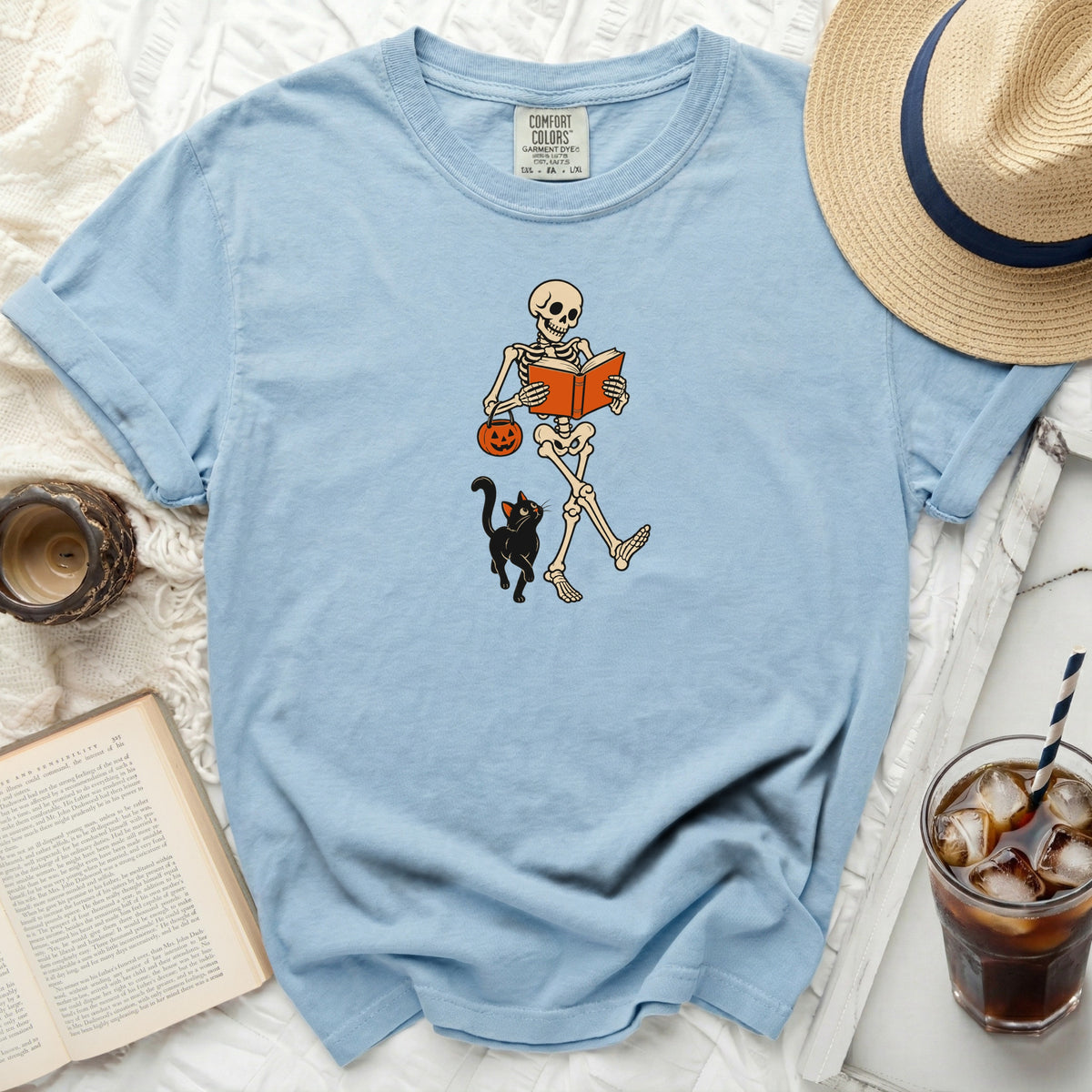 Light blue Comfort Colors t-shirt with a skeleton reading a book and holding a pumpkin basket.