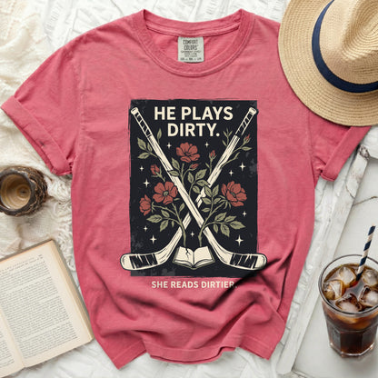 T-shirt with hockey sticks, book, and flowers; "HE PLAYS DIRTY. SHE READS DIRTIER."