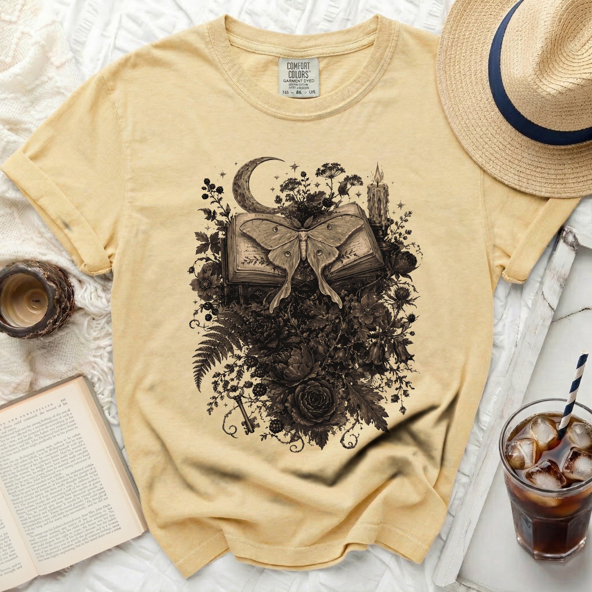 Yellow t-shirt with a black moth on open book surrounded by flowers and moon.