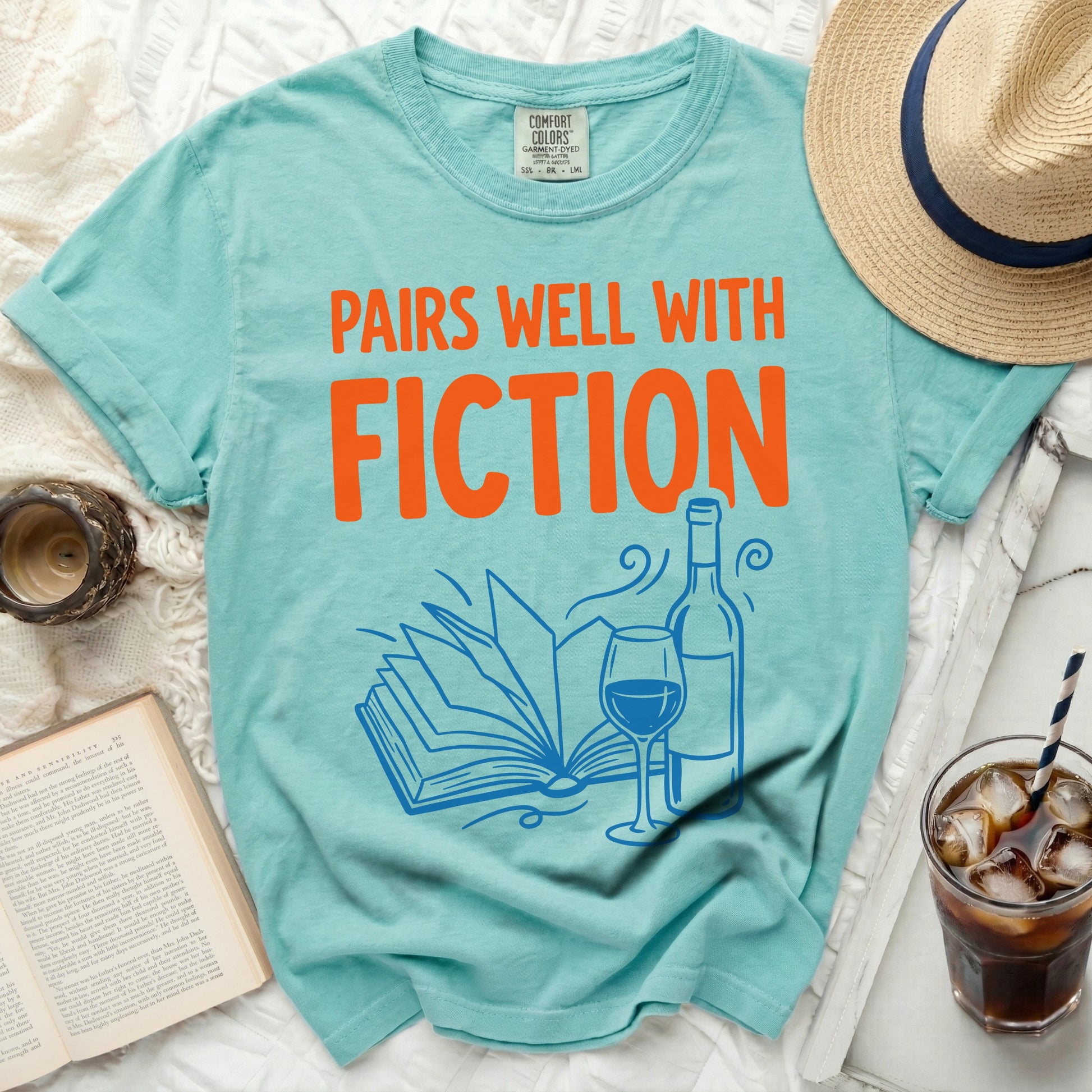 Teal t-shirt with "Pairs Well With Fiction" text and book illustration.