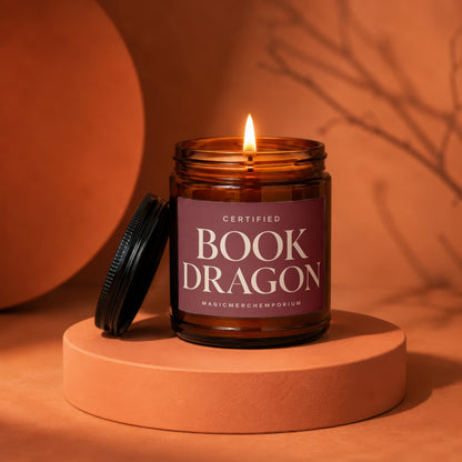 Amber glass candle with lit wick, "BOOK DRAGON" and "MAGICMERCHƐMPORIUM" text.