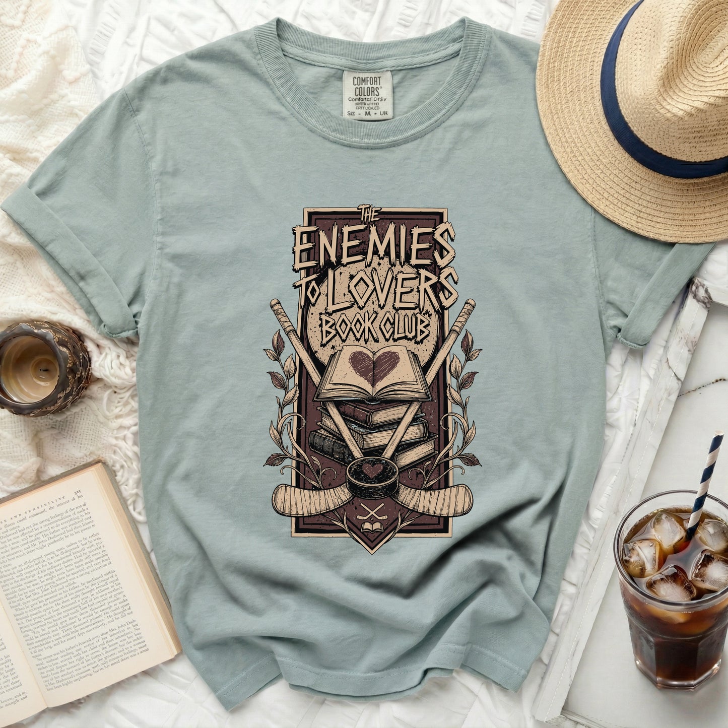 T-shirt with "The Enemies to Lovers Book Club" graphic and crossed hockey sticks.