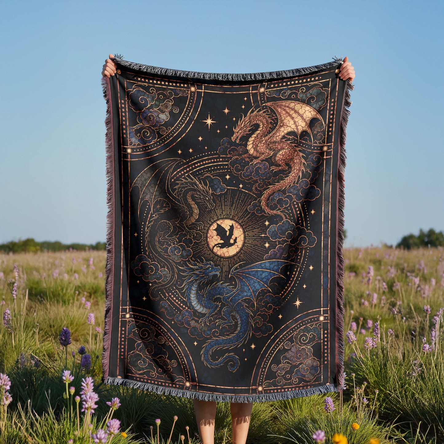 A person is holding up a large, intricately designed blanket with a dragon and star motif, standing in a field of purple flowers.
