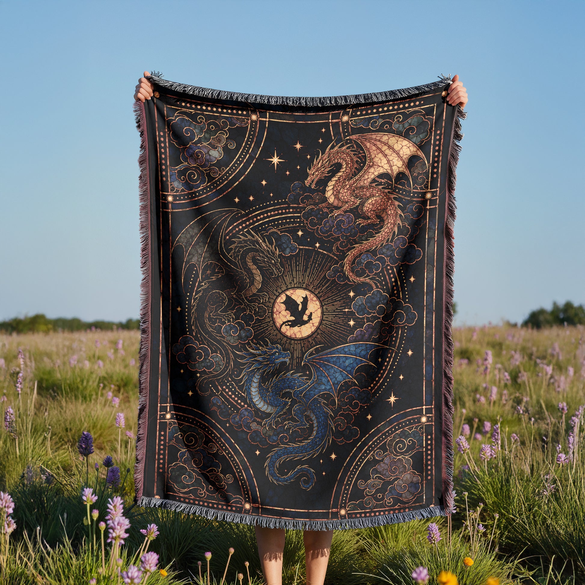 A person is holding up a large, intricately designed blanket with a dragon and star motif, standing in a field of purple flowers.