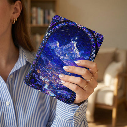 Person holding a book with stained glass art of a starry night over a city and mountains.