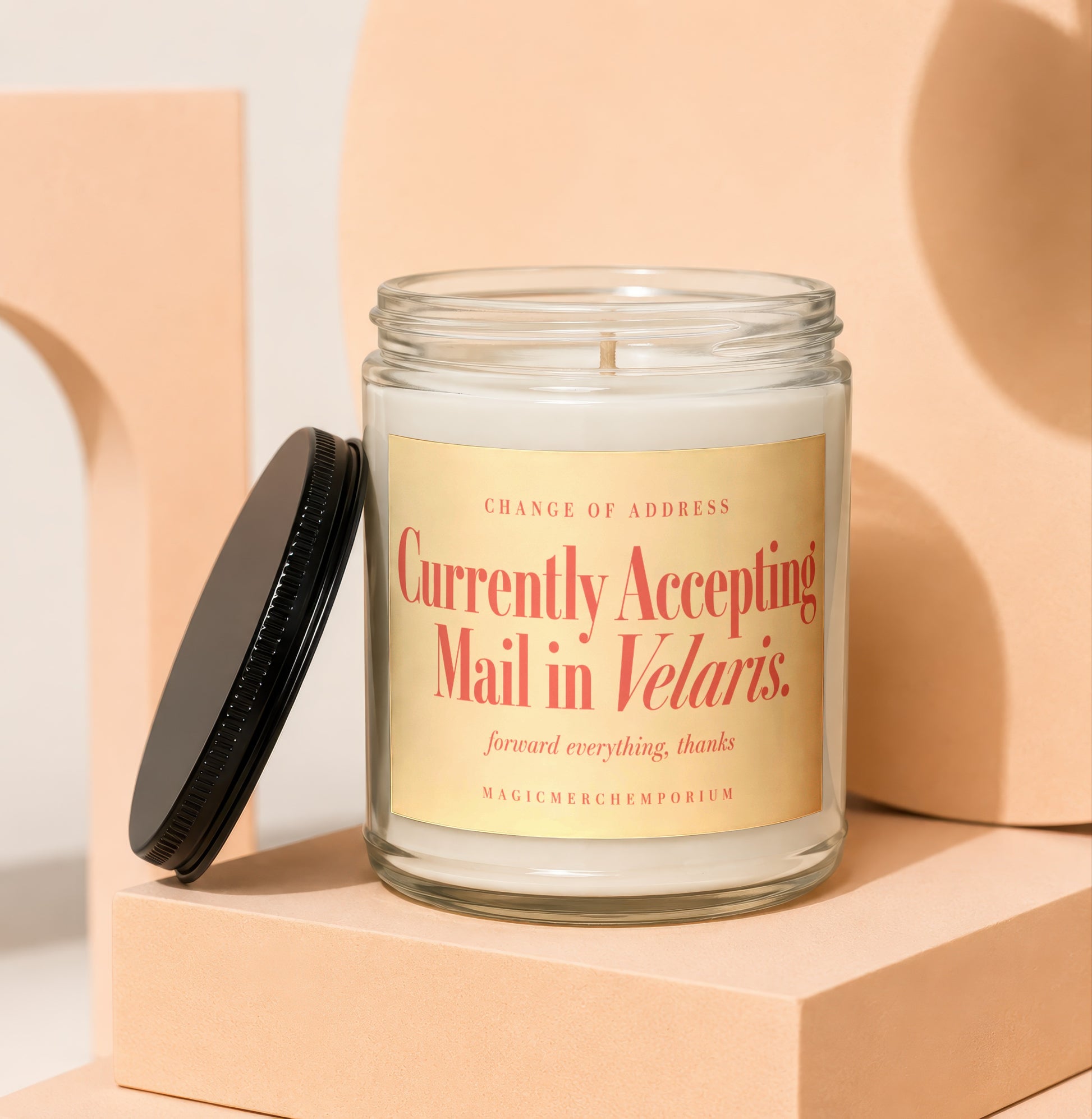 A glass candle jar with a black lid and a label reading "Currently Accepting Mail in Velaris."
