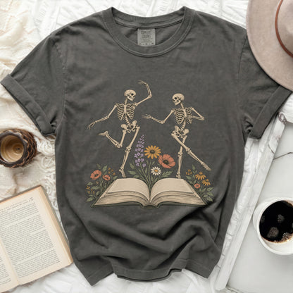 T-shirt with skeletons dancing around an open book and flowers.