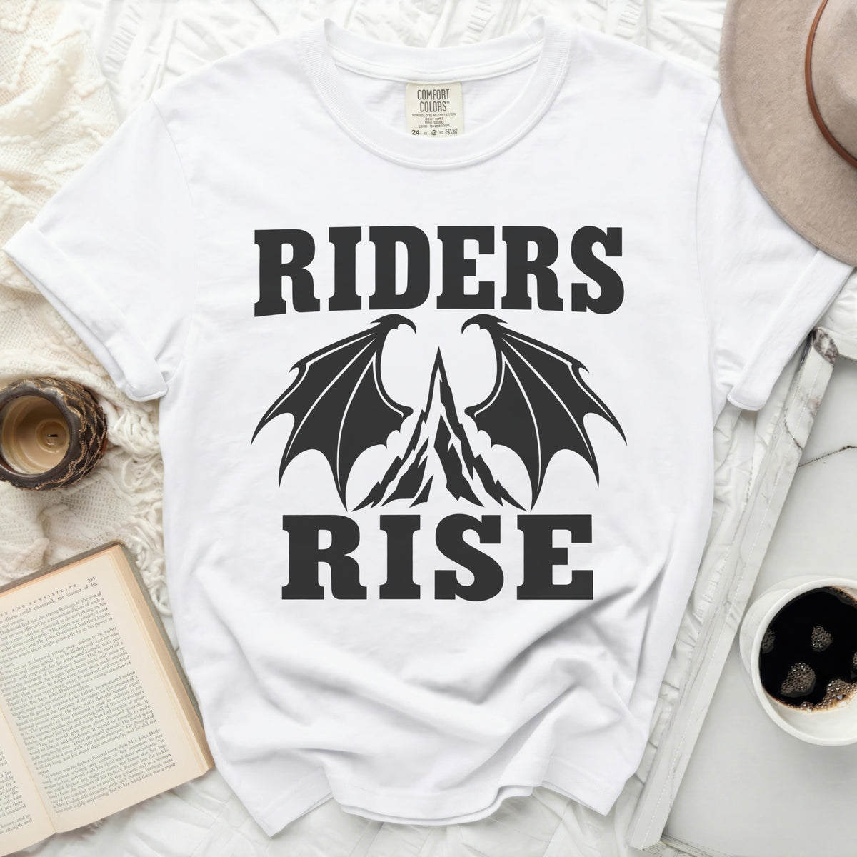 White t-shirt with black "RIDERS RISE" text and dragon wings over mountains graphic.
