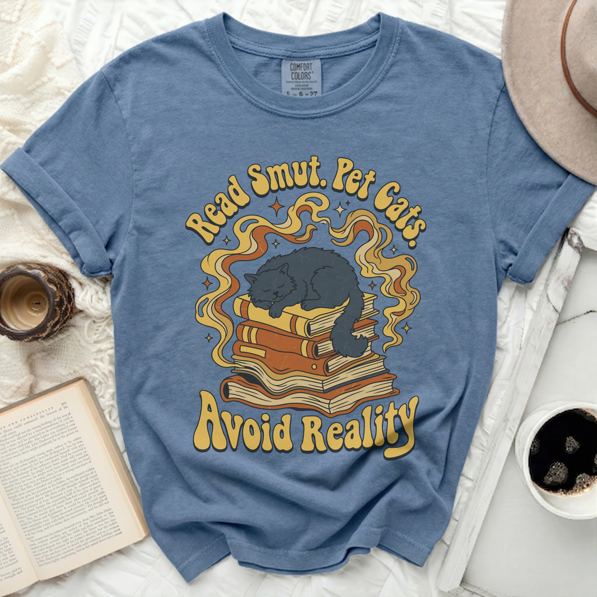 Blue t-shirt with a graphic of a cat sleeping on books, saying "Read Smut. Pet Cats. Avoid Reality."