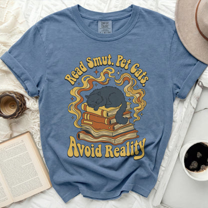 Blue t-shirt with a graphic of a cat sleeping on books, saying "Read Smut. Pet Cats. Avoid Reality."