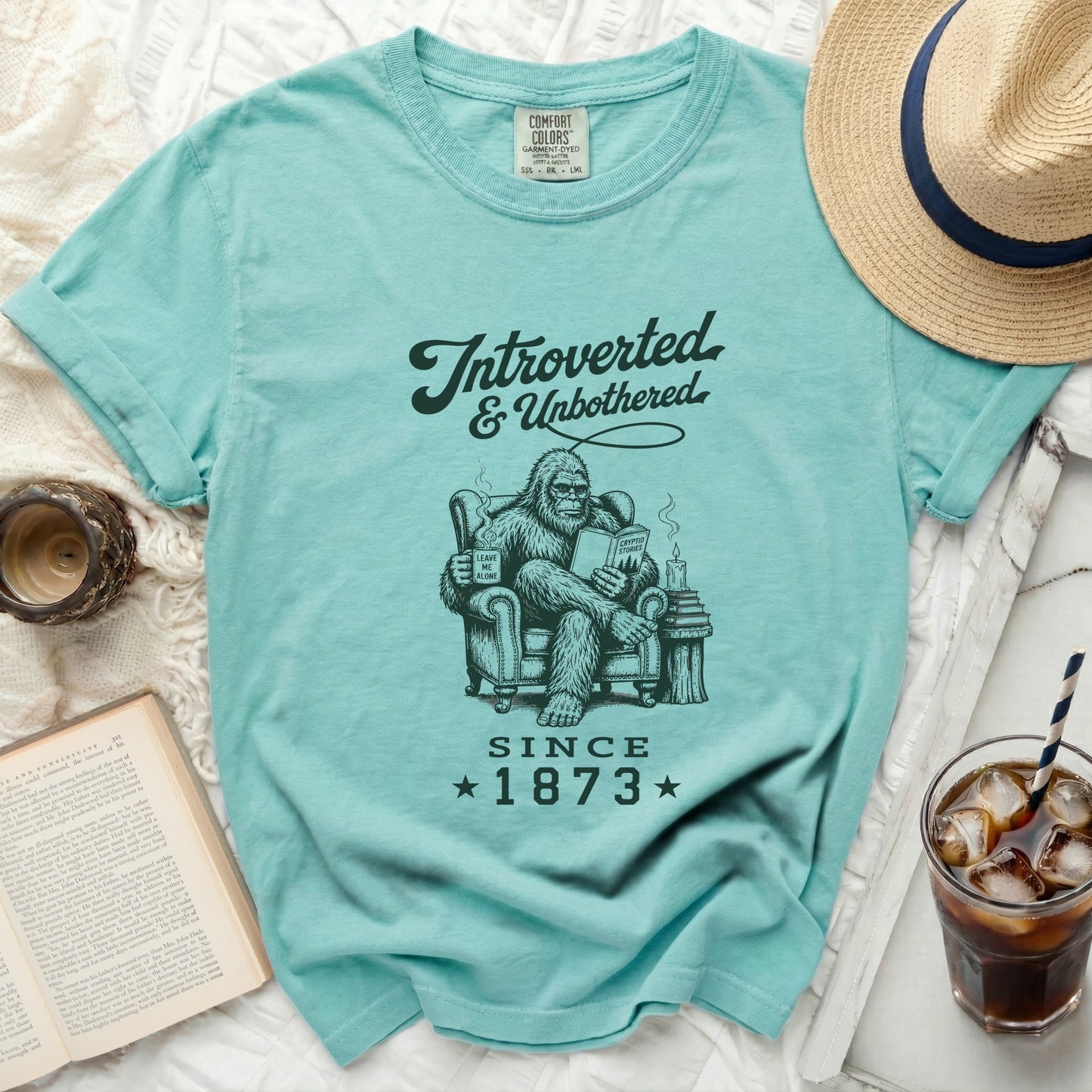 Bigfoot reading a book and mug that says "Leave Me Alone Since 1873."