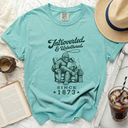 Bigfoot reading a book and mug that says "Leave Me Alone Since 1873."