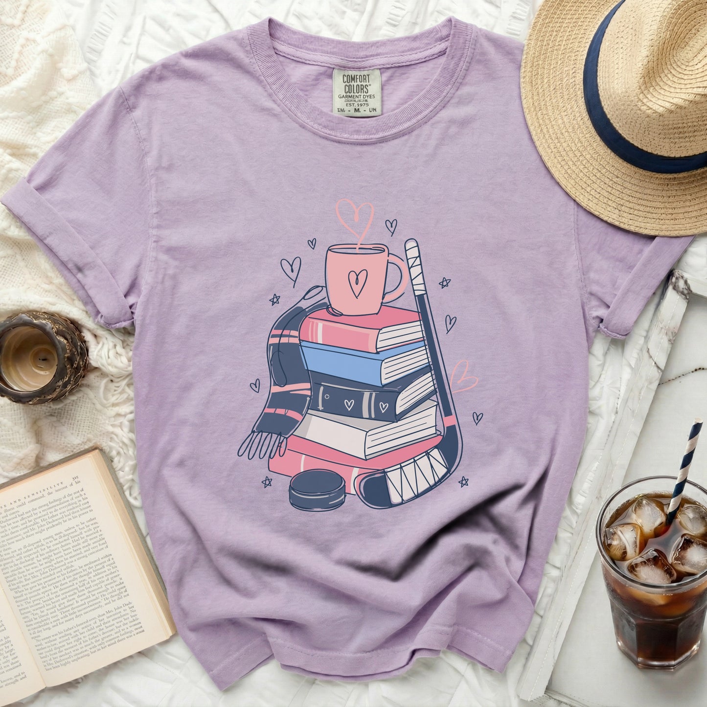 Purple t-shirt with stacked books, hockey stick, hearts, and mug graphic.