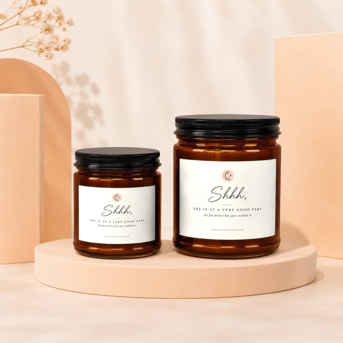 Two amber glass candles with black lids and white labels reading "Shhh, SHE IS AT A VERY GOOD PART".