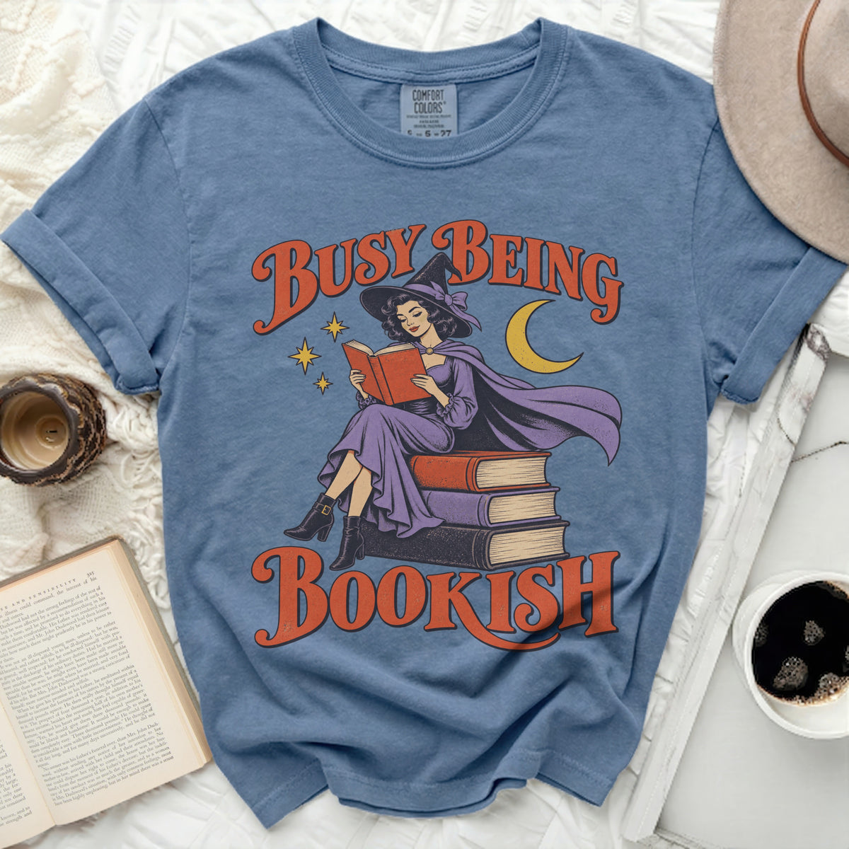 Blue t-shirt with "Busy Being Bookish" graphic of a witch reading.
