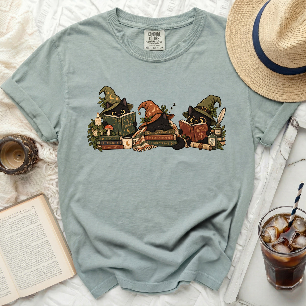 Three black cats in witch hats read books and nap amongst magical items.