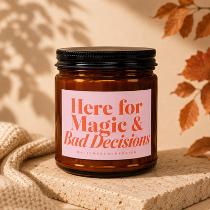 Amber candle in glass jar with pink label reading "Here for Magic & Bad Decisions."