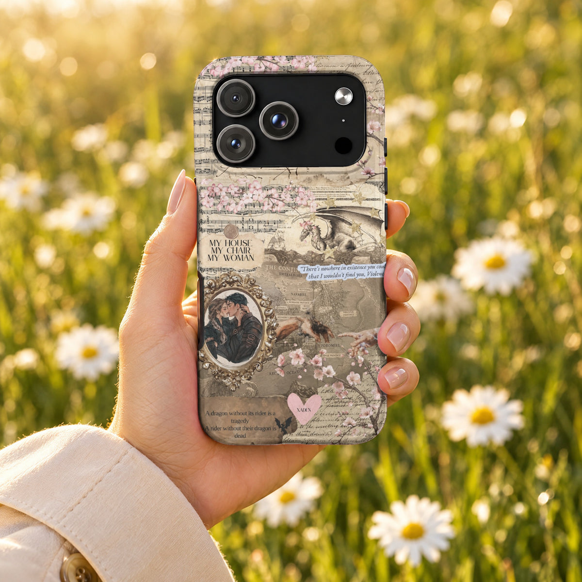 A hand holding a smartphone with a collage-style case featuring fantasy maps, romantic quotes, and dragons.