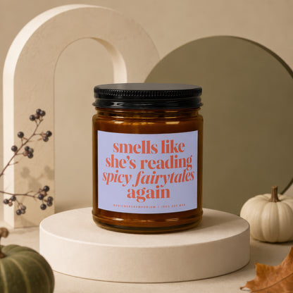 Amber jar candle with black lid, reads "smells like she's reading spicy fairytales again".