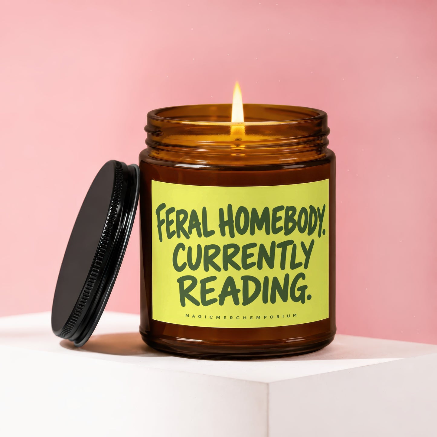 Amber jar candle with lit flame and black lid, labeled "Feral Homebody Currently Reading."