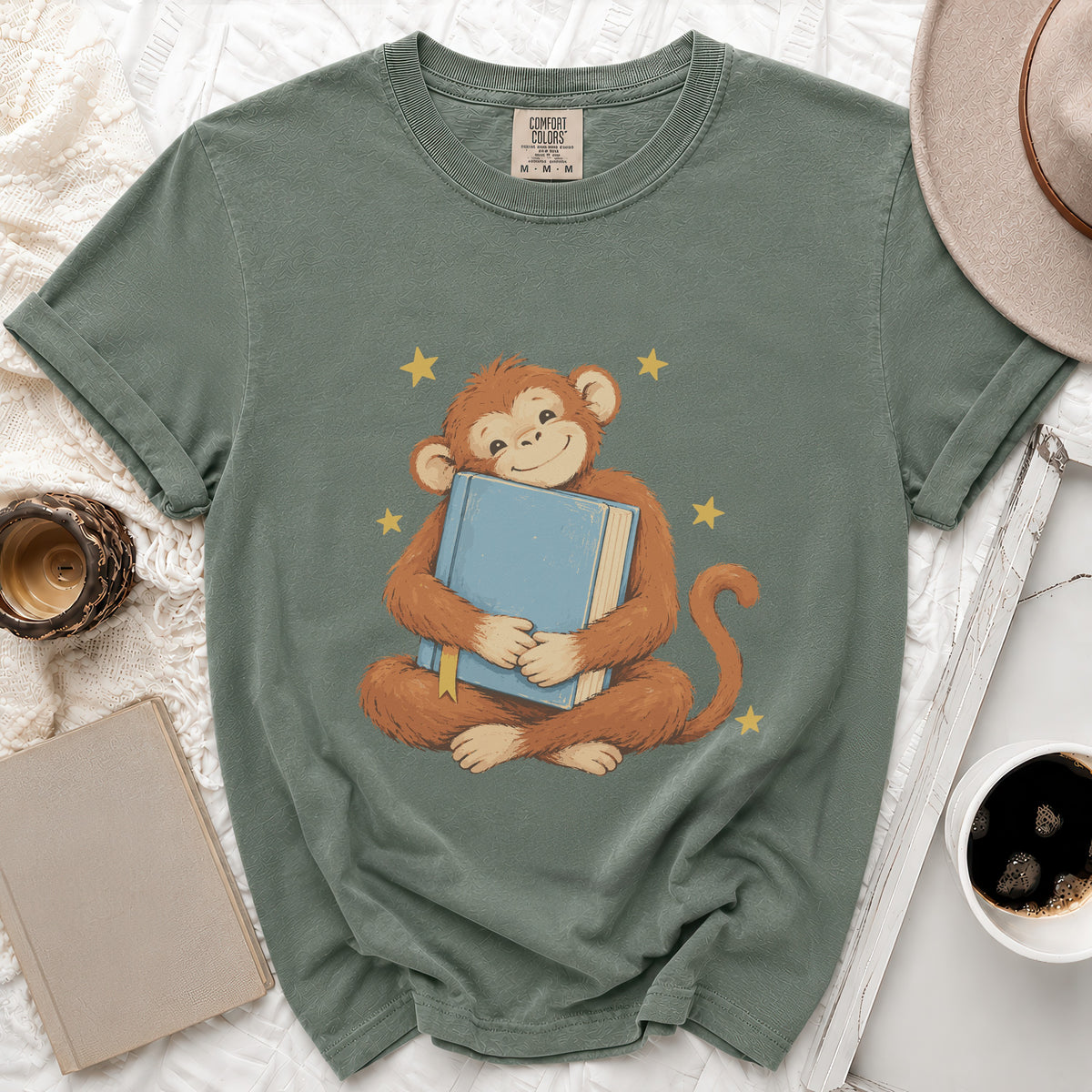 Green t-shirt with Comfort Colors tag, featuring a monkey hugging a blue book and yellow stars.