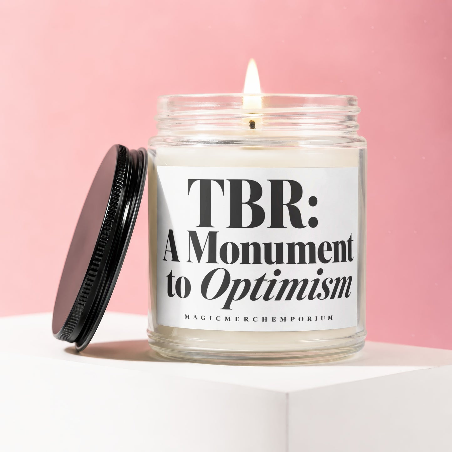 Lit candle in glass jar with lid off, labeled "TBR: A Monument to Optimism".