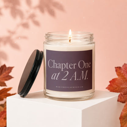 Lit candle with "Chapter One at 2 A.M." text on label, black lid off, autumn leaves.