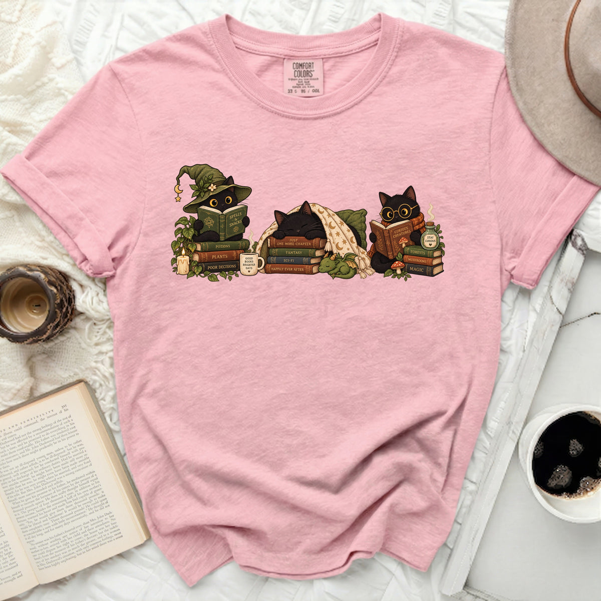 Pink t-shirt with illustration of three black cats reading books and wearing wizard hats.