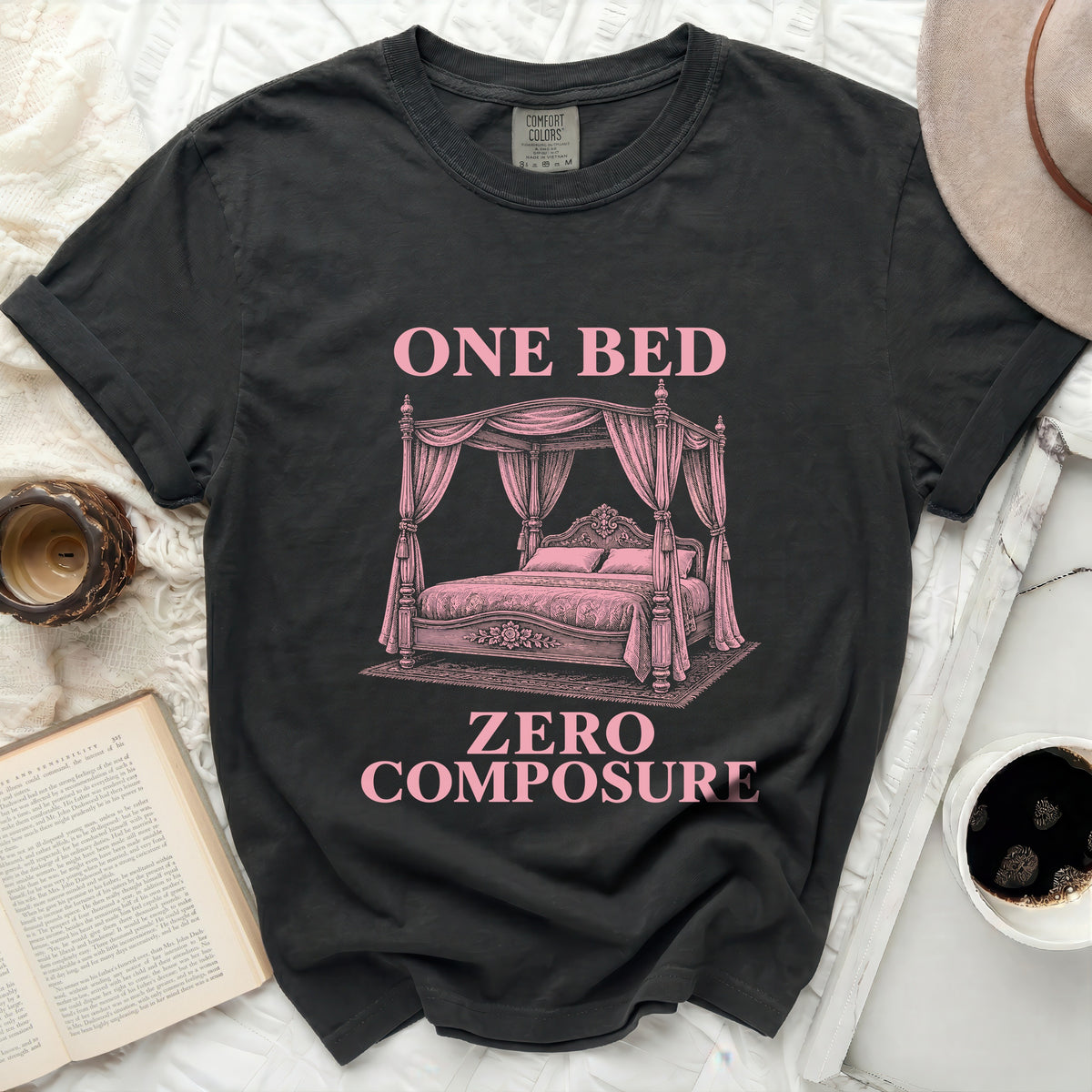 Dark t-shirt with pink text "ONE BED ZERO COMPOSURE" and a canopy bed graphic.