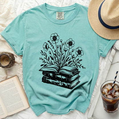 Teal t-shirt with black linework of opened books and a floral bouquet.