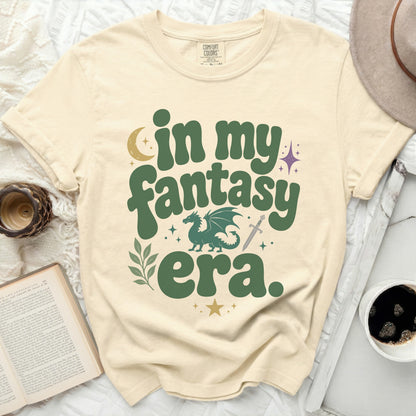 "In my fantasy era" text with dragon, sword, moon, and stars on a cream shirt.