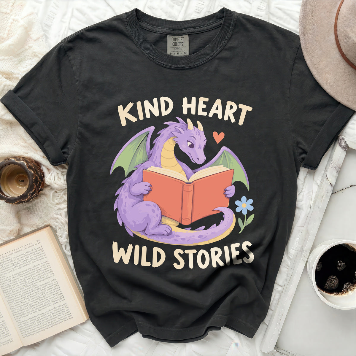 Black t-shirt with purple dragon reading a book, text "KIND HEART WILD STORIES".