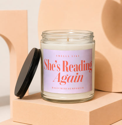 Glass candle with lavender label reading "She's Reading Again".