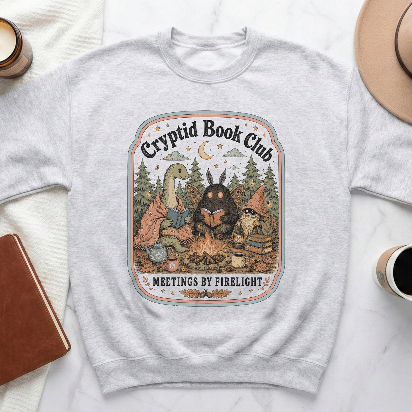 Cryptid Book Club featuring a dinosaur, mothman, and gnome around a campfire.
