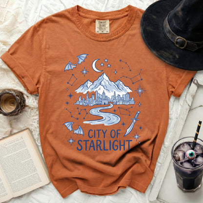 Orange t-shirt with "City of Starlight" graphic featuring city, mountains, moon, bats, and constellations.