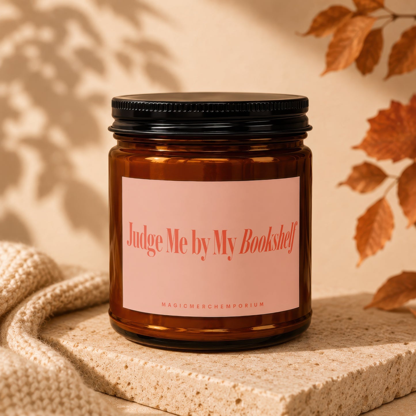 Amber candle with a pink label reading "Judge Me by My Bookshelf".
