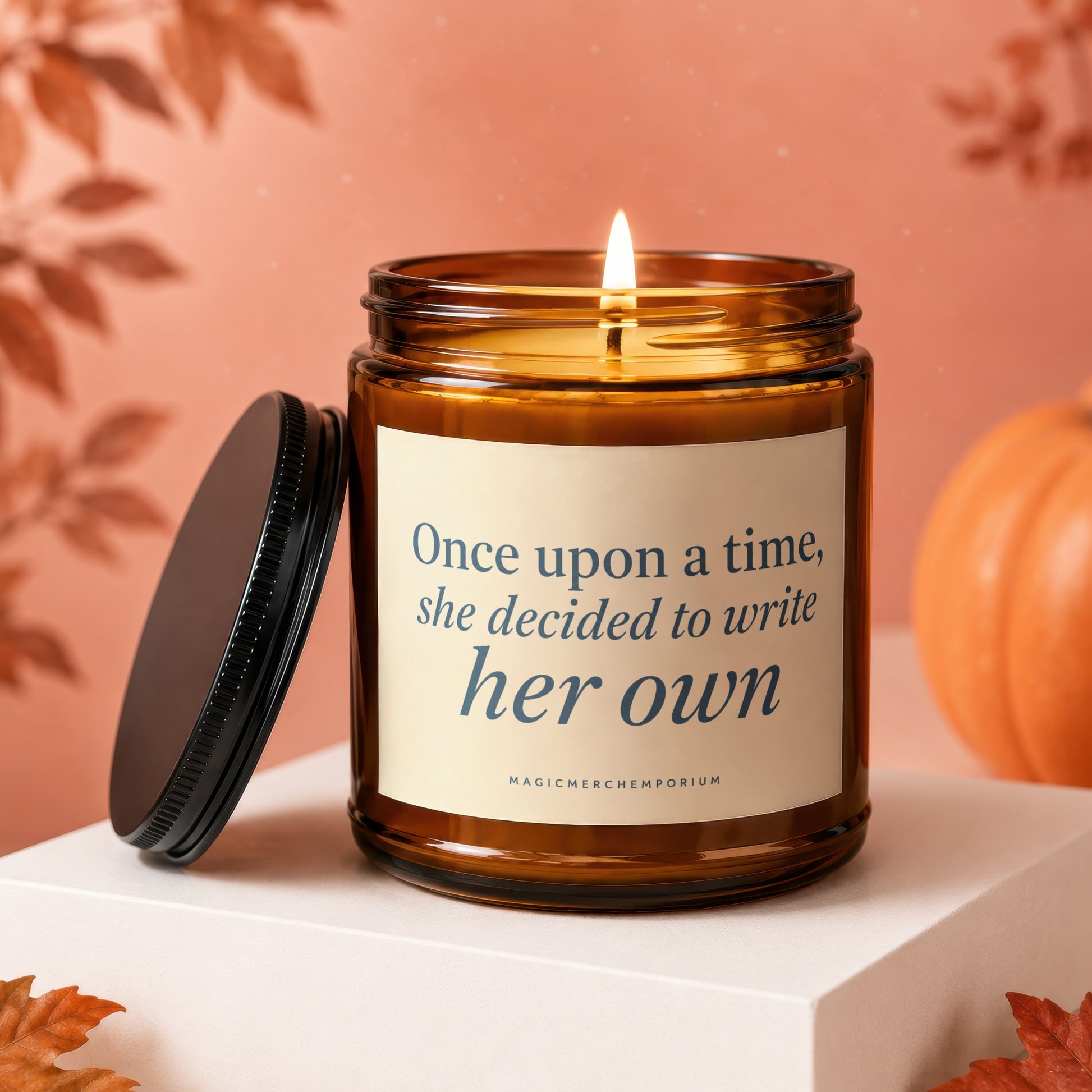 Amber candle with lit wick, black lid, and text "Once upon a time, she decided to write her own."