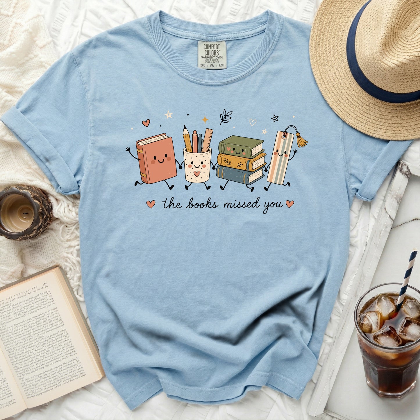Light blue t-shirt with cartoon books and a bookmark graphic saying "the books missed you".