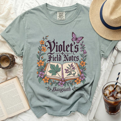 Dusty blue t-shirt with "Violet's Field Notes Basgiath" text and floral design.