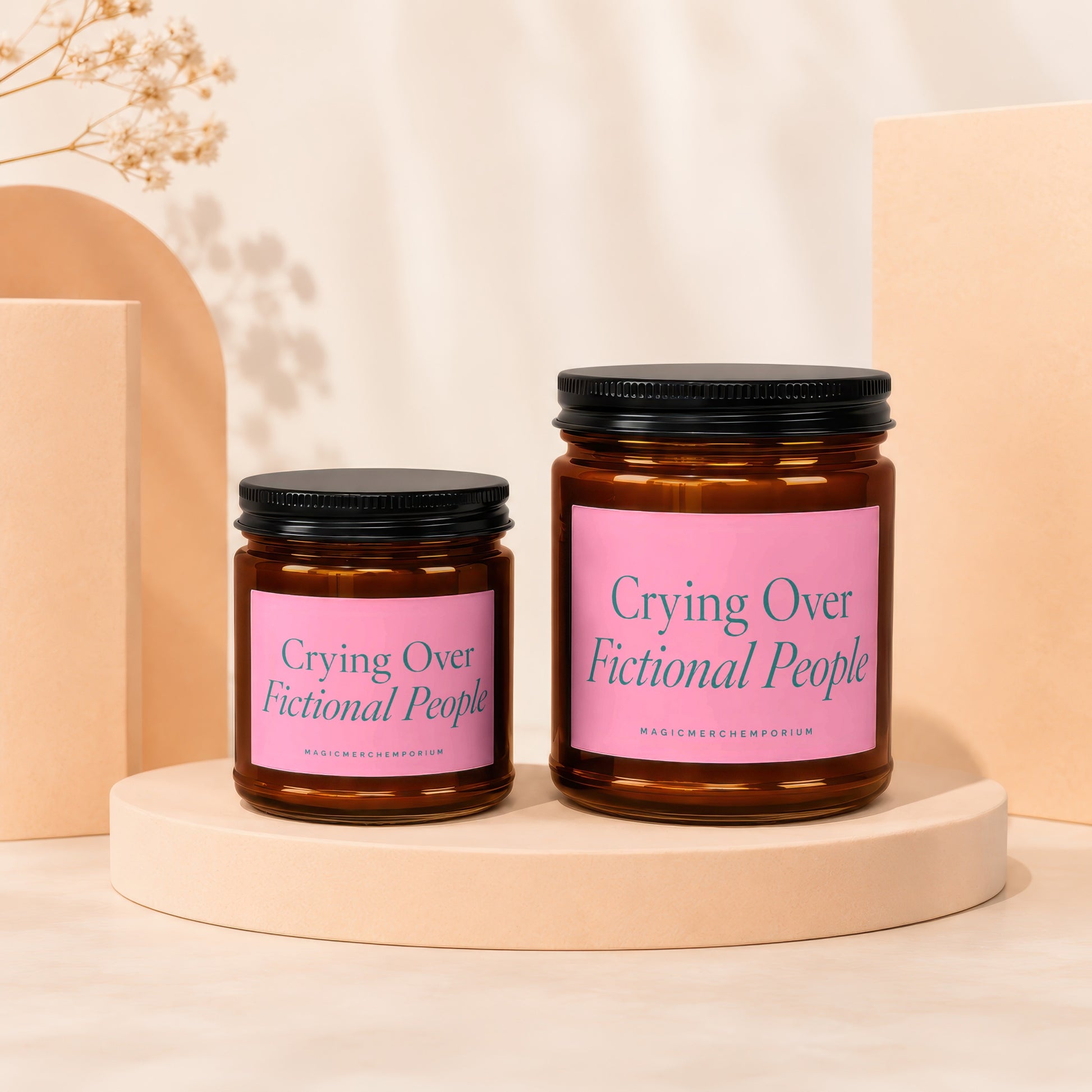 Two amber glass candles with pink labels reading "Crying Over Fictional People".