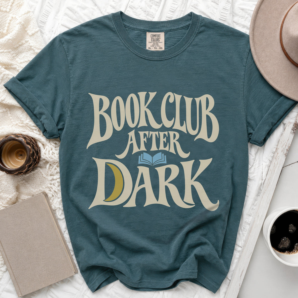 Dark teal t-shirt featuring cream text reading BOOK CLUB AFTER DARK with a blue open book and yellow crescent moon.