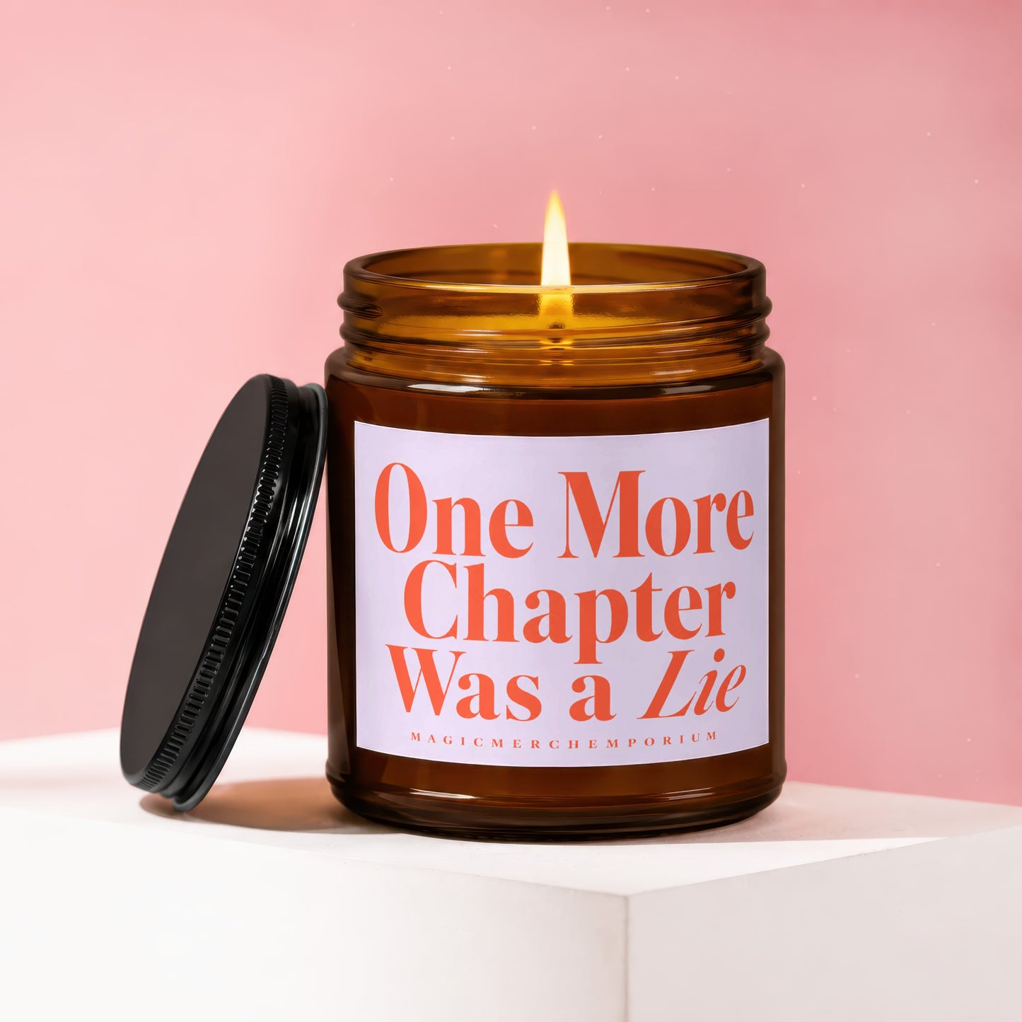 Amber glass candle with lit wick and black lid, reads "One More Chapter Was a Lie".