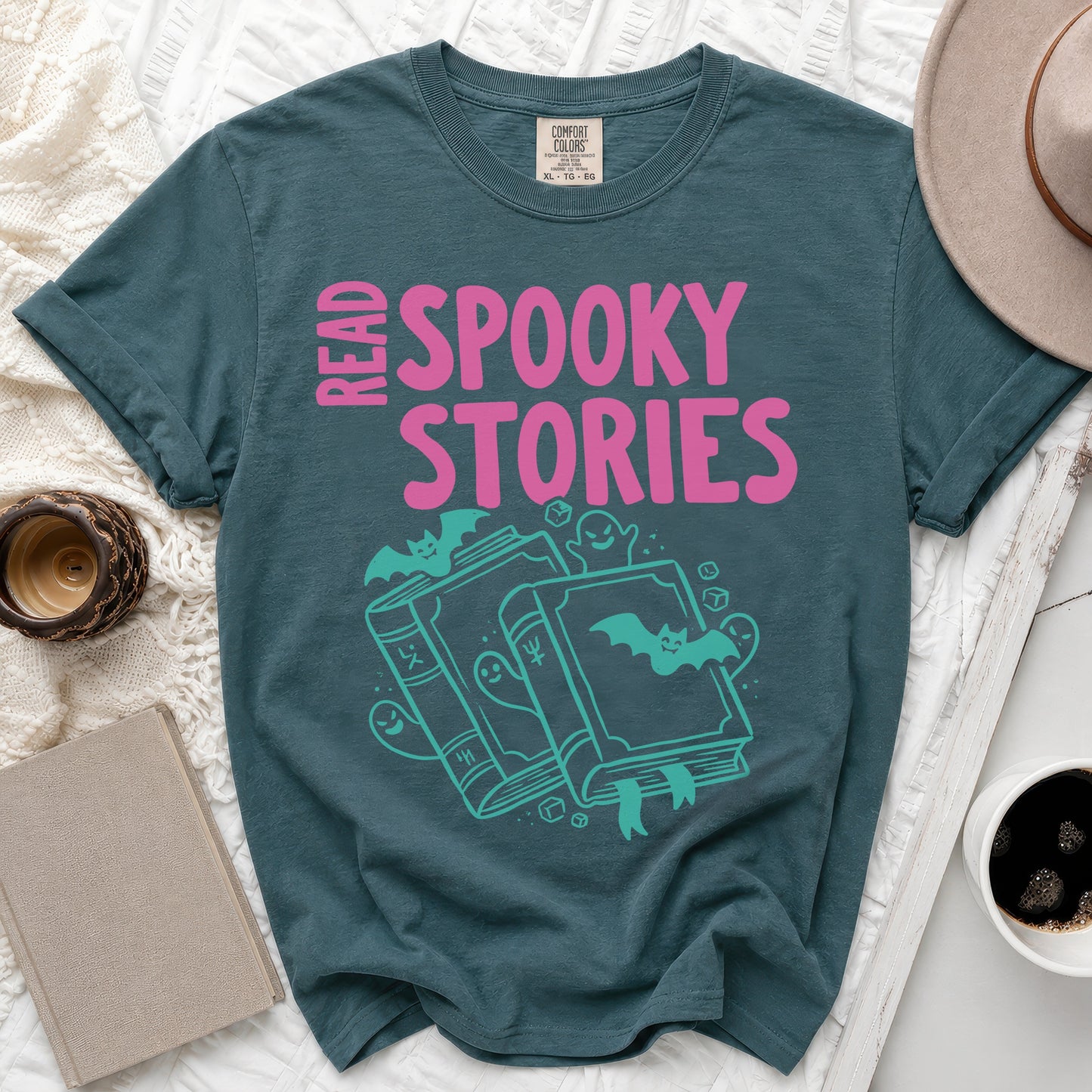 Teal t-shirt with pink "READ SPOOKY STORIES" text and teal illustrated books, bats, and ghosts.