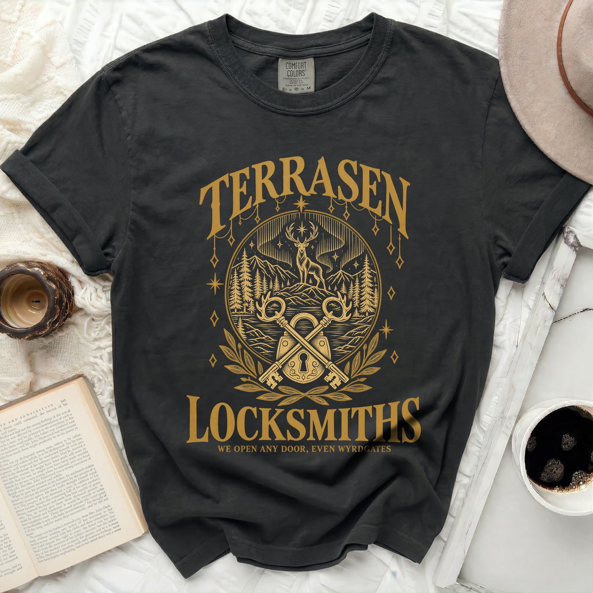Black t-shirt with gold graphic of a deer, mountains, keys, and text "TERRASEN LOCKSMITHS WE OPEN ANY DOOR, EVEN WYRDGATES".