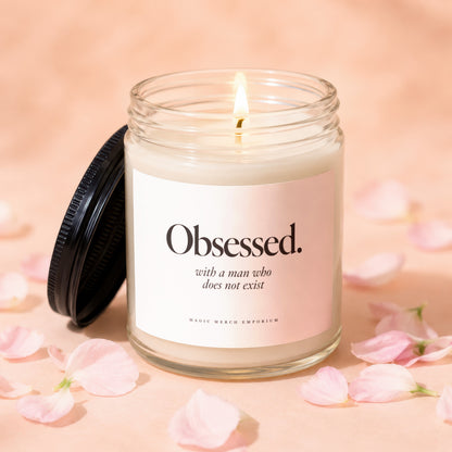 Glass candle with black lid, lit wick, and label that says "Obsessed. with a man who does not exist."