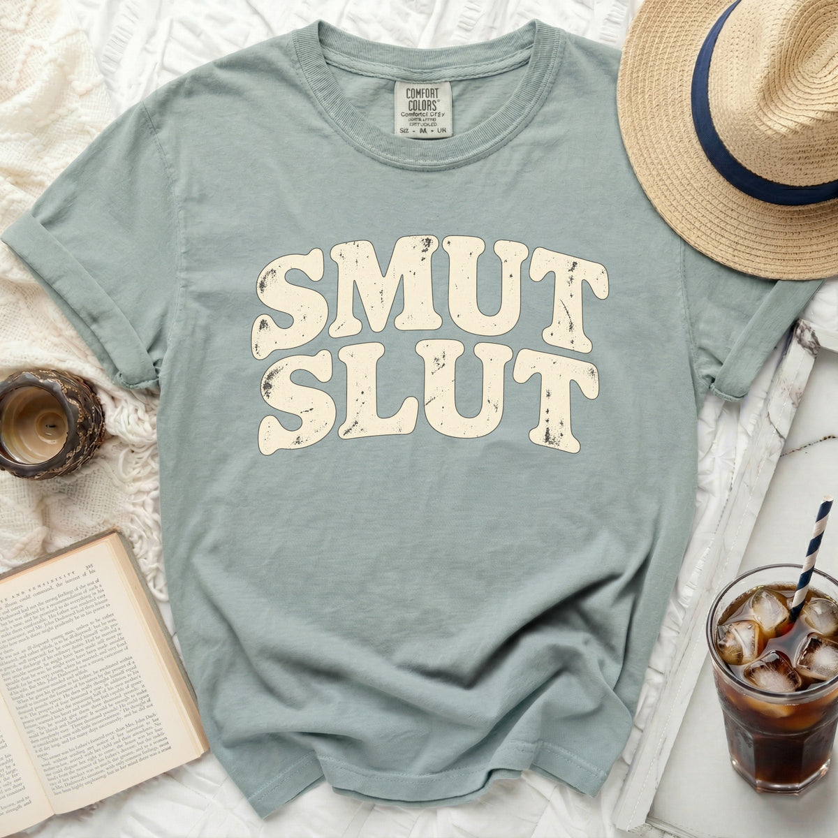 Light blue t-shirt with cream colored "SMUT SLUT" text and comfort colors tag.