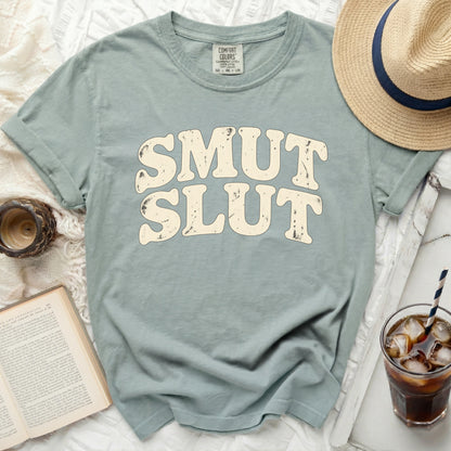 Light blue t-shirt with cream colored "SMUT SLUT" text and comfort colors tag.