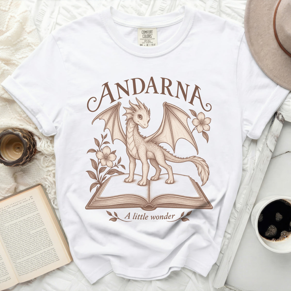 White t-shirt with a dragon on an open book. Text reads ANDARNA and A little wonder.