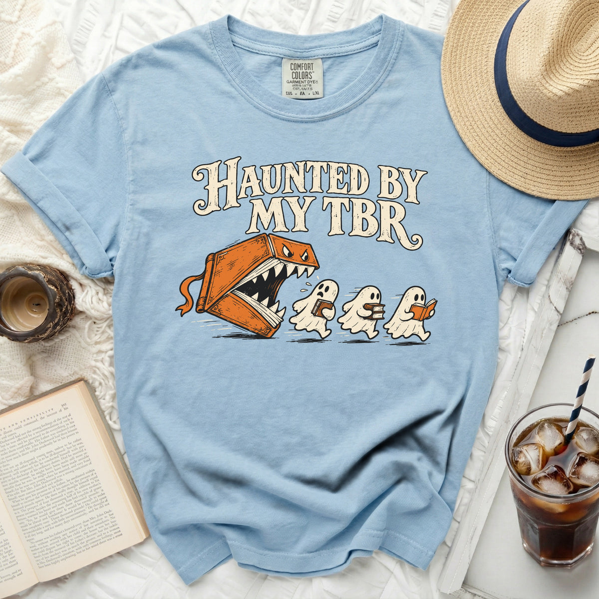Light blue t-shirt with "Haunted by My TBR" and illustrated book-eating monster chasing ghosts.